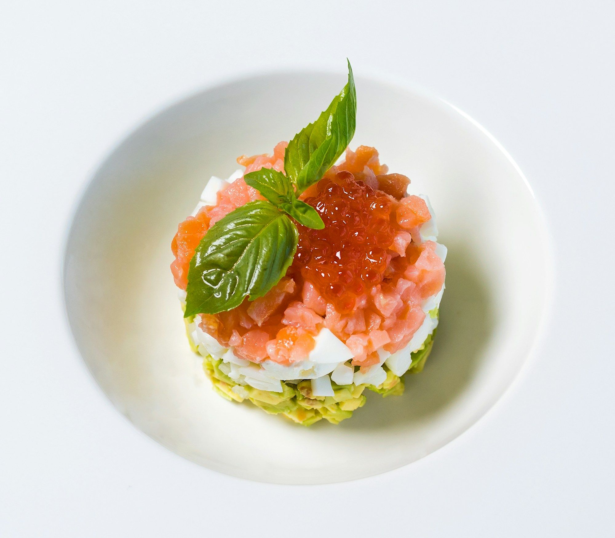 Tartare de saumon et œufs de truite sur avocat, dressé à l'emporte-pièce dans une assiette blanche