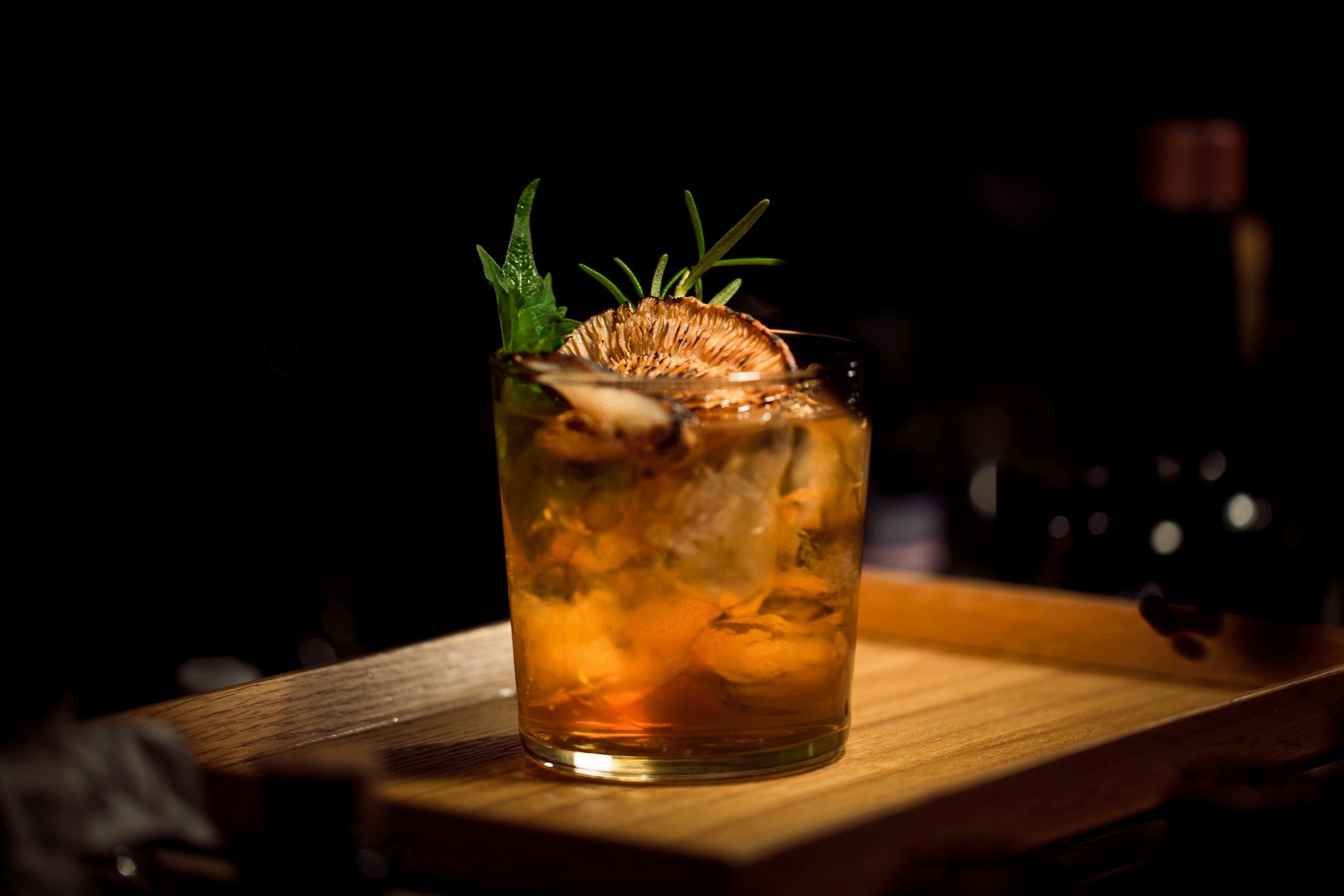 Cocktail ambré garni de romarin posé sur un comptoir en bois