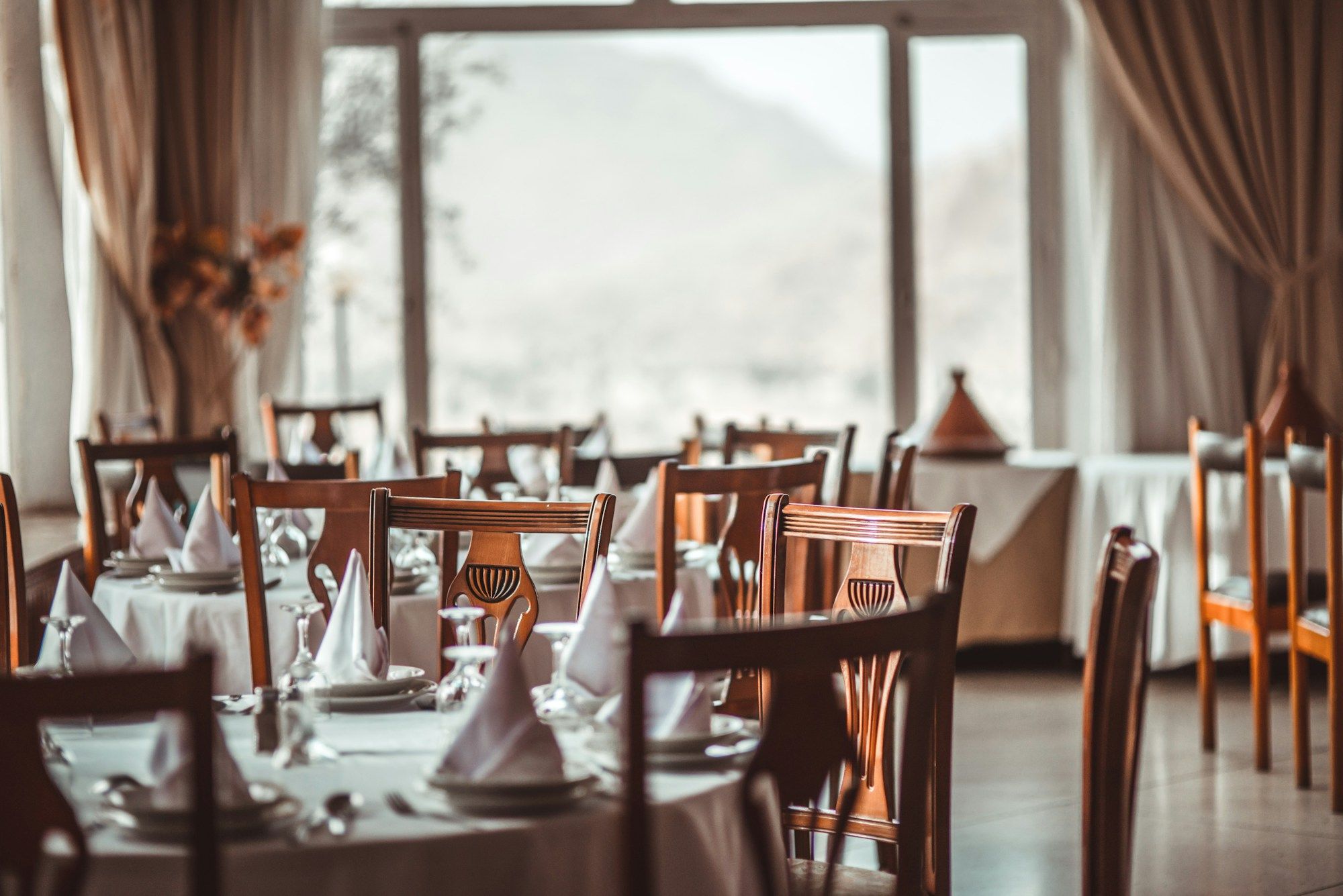 Salle de restaurant baignée de lumière naturelle, tables dressées près des fenêtres