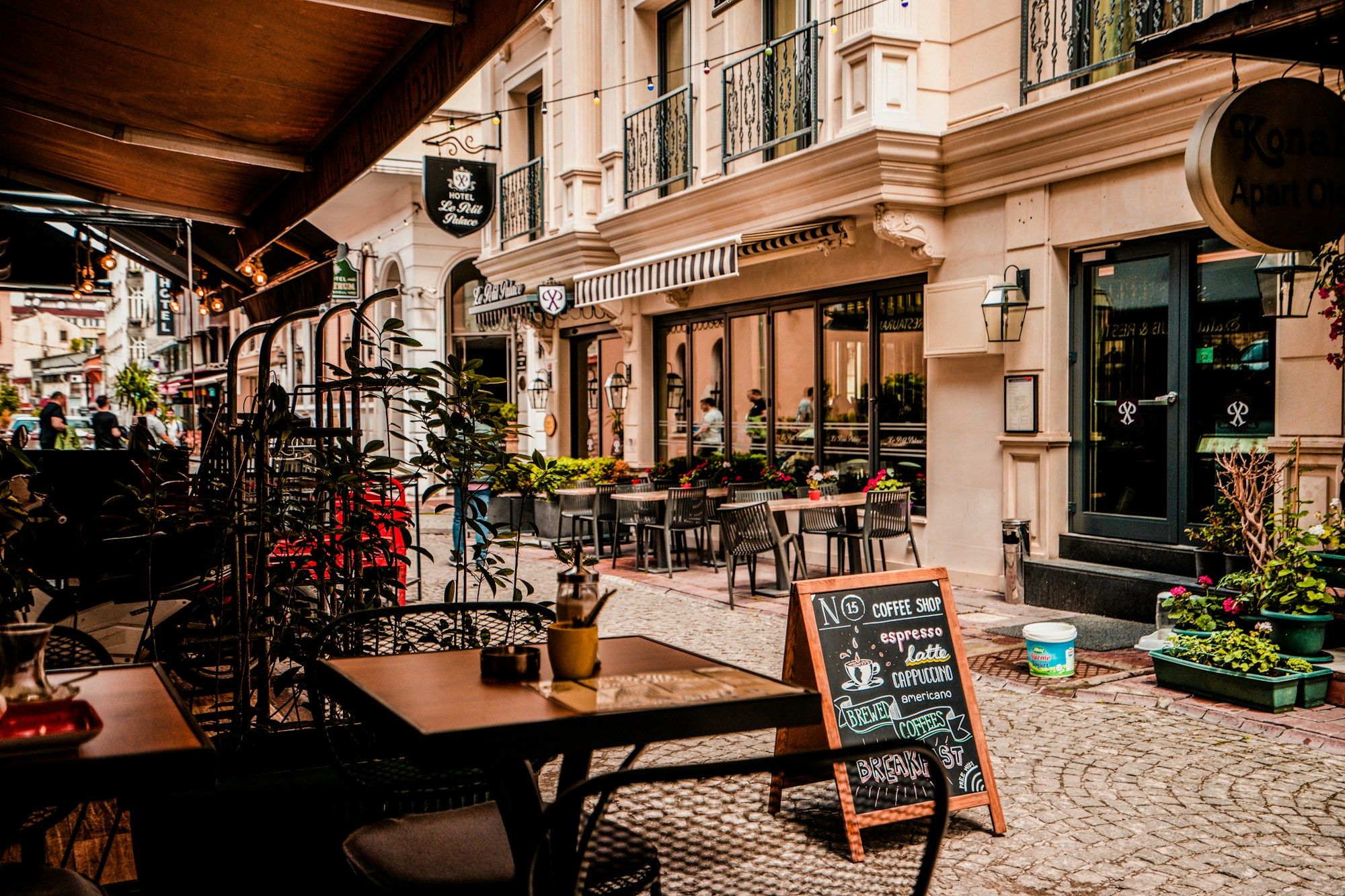 Terrasse de restaurant en bord de rue pavée, avec tables et ardoise
